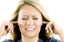 An Image of a woman with her fingers in her ears ans a distressed look as if she is experienceing tinnitus.